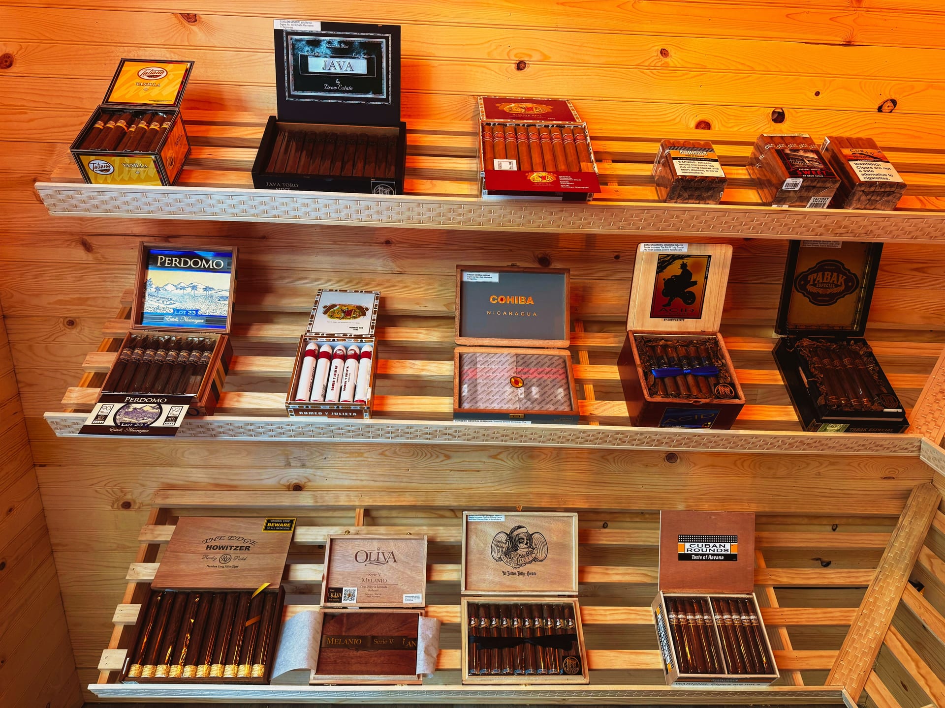 Premium boxed cigars including Cohiba, Perdomo, and Oliva on wood shelves.